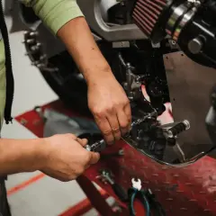 Mecánico realizando el cambio de aceite a una moto, usando herramientas para acceder al motor.