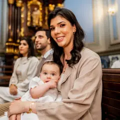 Elegancka stylizacja na chrzciny jesienią: młoda mama z dzieckiem w kościele, w tle rodzina i goście.