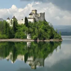 Zamek w Niedzicy dumnie wznosi się na wzgórzu nad jeziorem, odbijając się w spokojnej tafli wody.
