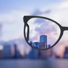 Okulary progresywne co to? Widok miasta przez soczewki, które wyostrzają perspektywę, pokazując wyraźne budynki na tle zachodzącego słońca.