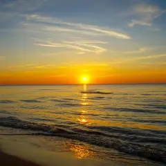 Piękny plaża zachód słońca nad spokojnym morzem. Słońce odbija się w wodzie, tworząc złoty szlak.