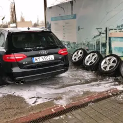Czarny Audi na myjni bezdotykowej, obok cztery koła. Poznaj myjnia bezdotykowa triki, by Twój samochód lśnił!