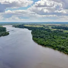 Szeroka Wisła, najdłuższa rzeka w Polsce, płynie przez zielone tereny z widoczną w oddali panoramą miasta.