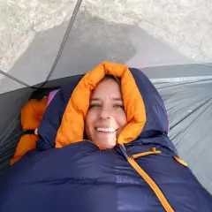Smiling woman bundled in a navy and orange rei magma 15 weight sleeping bag inside a tent.