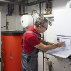 Ein Mann in Latzhose führt eine Emissionsmessung an einer Heizungsanlage durch. Der Schornsteinfeger prüft die Werte am Display.