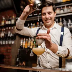 Uśmiechnięty barman przelewa drinka przez sitko. Czy barman może pić w pracy? Ten z pewnością tworzy pyszne koktajle!