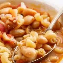 Un cucchiaio raccoglie un saporito piatto di pasta e fagioli, con maccheroni, fagioli bianchi e pomodoro in un brodo ricco.