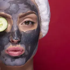 Donna con maschera viso all'argilla e fetta di cetriolo sull'occhio. La maschera viso a cosa serve? A purificare e rinfrescare la pelle.