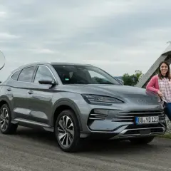 Mujer sonríe junto a un BYD Seal U, disfrutando del dm-i comfort en un día nublado, con antenas parabólicas de fondo.