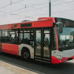 Czerwony autobus miejski jedzie po moście, w tle widać drzewa i błękitną poręcz. To idealny środek transportu, by dojechać nad morze.