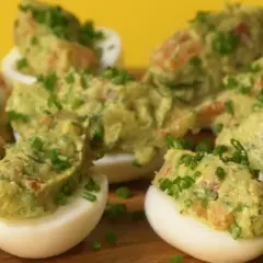 Jajka faszerowane guacamole, udekorowane szczypiorkiem, wyglądają apetycznie na drewnianej desce.