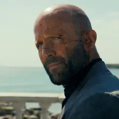 En skadad man med skägg och rakad skalle, klädd i kavaj, blickar ut över havet. En scen från biodlaren film.