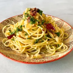 Un plato de spaghetti aglio e olio, con ajo laminado, perejil fresco y hojuelas de chile rojo, servido en un plato decorado.