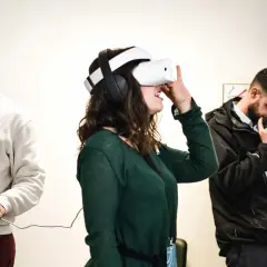 Kobieta w goglach VR doświadcza wirtualnej rzeczywistości, pokazując, jak działa vr. Obok stoją mężczyźni, jeden z telefonem.