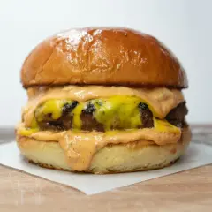 Soczysty burger z roztopionym serem i sosem na jasnym tle.