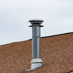 Cheminée sans tubage sur un toit brun sous un ciel couvert. La cheminée est en métal avec un chapeau ventilé.