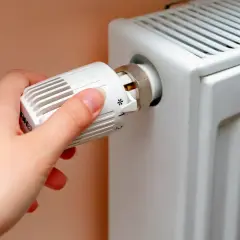 Dłoń reguluje termostat grzejnika.