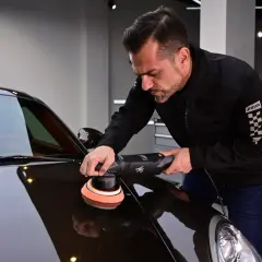 Man polerar en mörk bil med en polermaskin. En demonstration av hur polerar man en bil för att få en spegelblank yta.