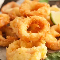 Crujientes calamars a la romana, dorados y listos para disfrutar, acompañados de gajos de limón y perejil fresco.