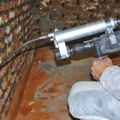 Person im Schutzanzug führt ein Injektionsverfahren selber machen durch, um eine feuchte Wand zu sanieren.
