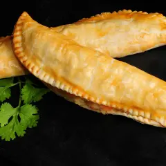 Dos empanadas de salmón doradas y crujientes, con un toque de cilantro fresco sobre fondo negro.