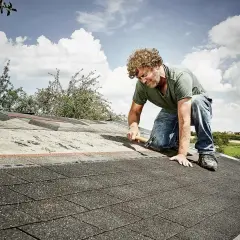 Mann verlegt mit Hammer und Nägeln neue dachschindeln auf einem Hausdach.