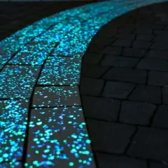 Ścieżka z luminescencyjnej kostki wokół pomnika, nocą mieniąca się błękitno-zielonym blaskiem.