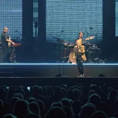 Ein Musiker mit goldenem Sakko singt auf der Bühne, umgeben von seiner Band. Ein Konzert von Simply Red in Stuttgart.