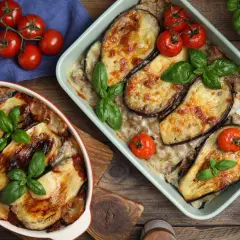Deux plats d'aubergine à la parmesane au four, dorés et gratinés, garnis de tomates cerises et de basilic frais.