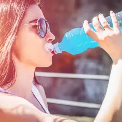 Kobieta w okularach przeciwsłonecznych pije niebieski izotonik z plastikowej butelki, nawadniając się w słoneczny dzień.
