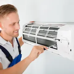 Un technicien ajuste un climatiseur mural. Il s'assure que l'appareil fonctionne bien pour éviter toute mauvaise odeur de climatisation.