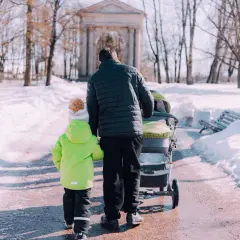 Ojciec z dziećmi spaceruje po zaśnieżonym parku. Pamiętaj, przy jakiej temperaturze nie wychodzić z dzieckiem latem, by uniknąć przegrzania.