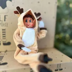 Uroczy elf w stroju renifera z uszkami i brązowymi rogami siedzi na kartonie z napisem "Elf na półce".