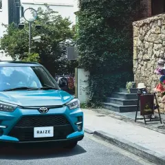 Turkusowy Toyota Raize parkuje na wąskiej uliczce z kamienną ścianą i wystawą kapeluszy.