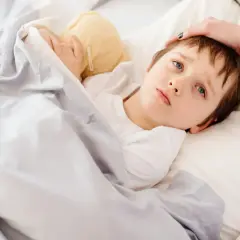 Chory chłopiec z pluszakiem pod kołdrą, czuje się lepiej po podaniu **Panadol**.