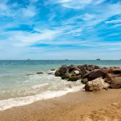 Olas rompiendo en la arena dorada de la playa Quitapellejos. El mar turquesa se extiende hasta el horizonte, con barcos navegando. ¡Un lugar ideal para relajarse!