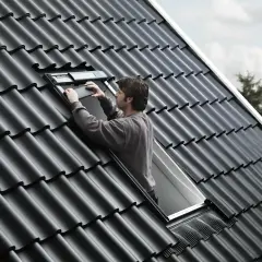 Uomo sul tetto che installa una finestra, la casa prende luce dal tetto.