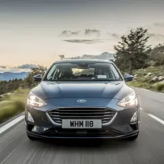 Ciemny Ford Focus MK5 jedzie krętą drogą wśród gór. Słońce zachodzi, tworząc piękne niebo.
