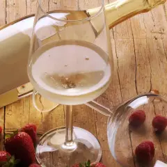 Butelka i kieliszek pełne musującego płynu, obok truskawki i maliny. To jest prosecco, idealne na letnie popołudnie.