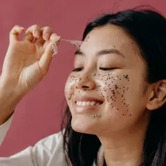 Kobieta z uśmiechem zdejmuje z twarzy błyszczący peeling do suchej skóry.