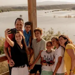 Familia sonriente se toma un selfie con un lago de fondo. Un día perfecto en la playa de Vera para niños, explorando la naturaleza.