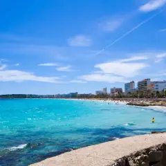 En livlig Cala Millor Beach med turkost vatten, solbadande människor och hotell längs kusten under en klarblå himmel.