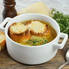 Jak zrobić zupę cebulową? Aromatyczna zupa cebulowa z grzankami i serem, podana w białej miseczce, z gałązką tymianku.