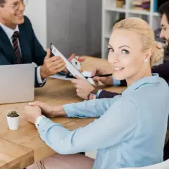 Uśmiechnięta kobieta przy stole z dokumentami, gdzie omawiany jest poręczenie kredytu.