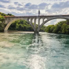 Ponte ad arco su fiume con acque di colori diversi, dove si intravedono segnali navigazione fluviale.