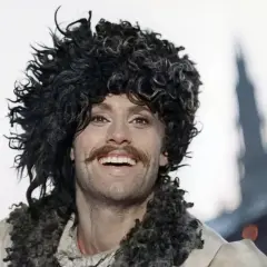Daniel Olbrychski w filmach, z charakterystyczną burzą loków i wąsami, uśmiecha się szeroko.