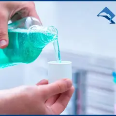 Mano versa collutorio blu in un bicchierino. Attenzione: la clorexidina macchia i denti.
