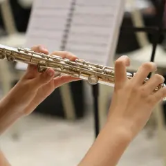 Dłonie grają na instrumencie podobnym do fletu, z nutami w tle.