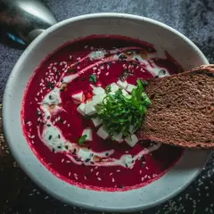 Un bol de soupe de betterave rouge polonaise, garni de crème, de dés de fromage et d'herbes, avec du pain de seigle.