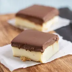 Zwei rechteckige Stücke schokokuchen mit vanillepudding, bedeckt mit Schokolade, auf einem Holzbrett.